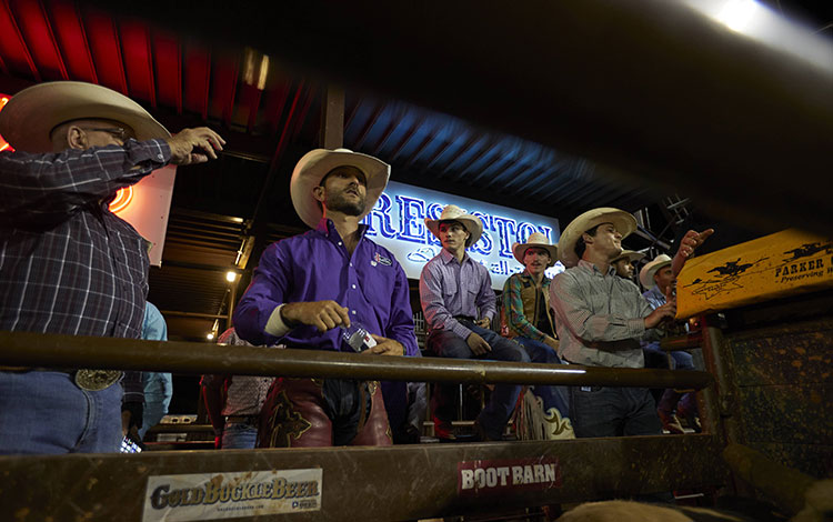 Man surrounded by people on the bucking chutes at a rodeo getting ready to ride bulls.